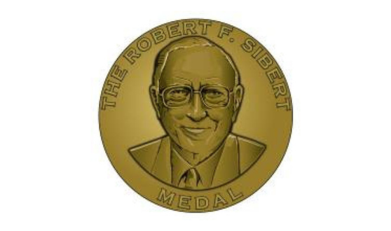 Gold seal with a man with glasses and text The Robert F. Sibert Medal