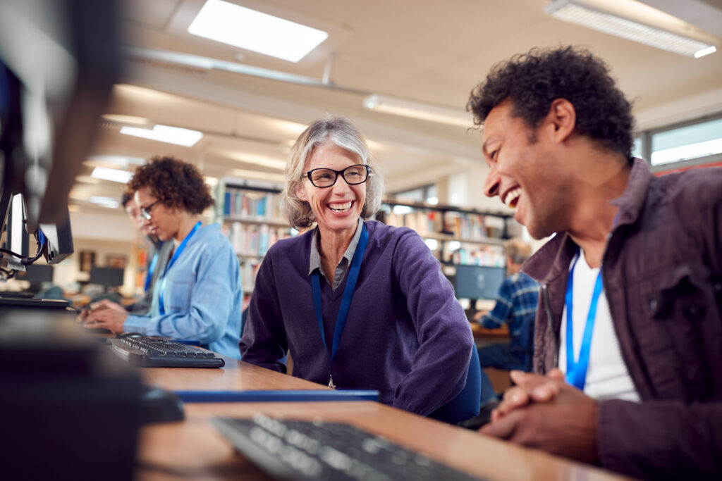 Teacher With Group Of Mature Adult Students In Class Working At Computers In College Library