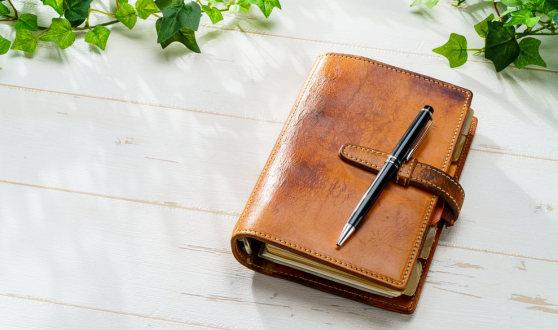 Leather bound notebook with a pen on top of it on table with ivy