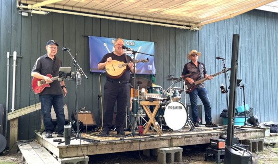 Three men on an outdoor stage with guitars and drums